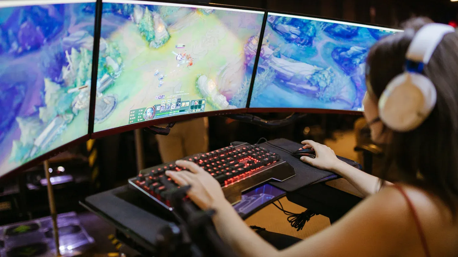A young woman using a gaming keyboard to play across a three monitor setup