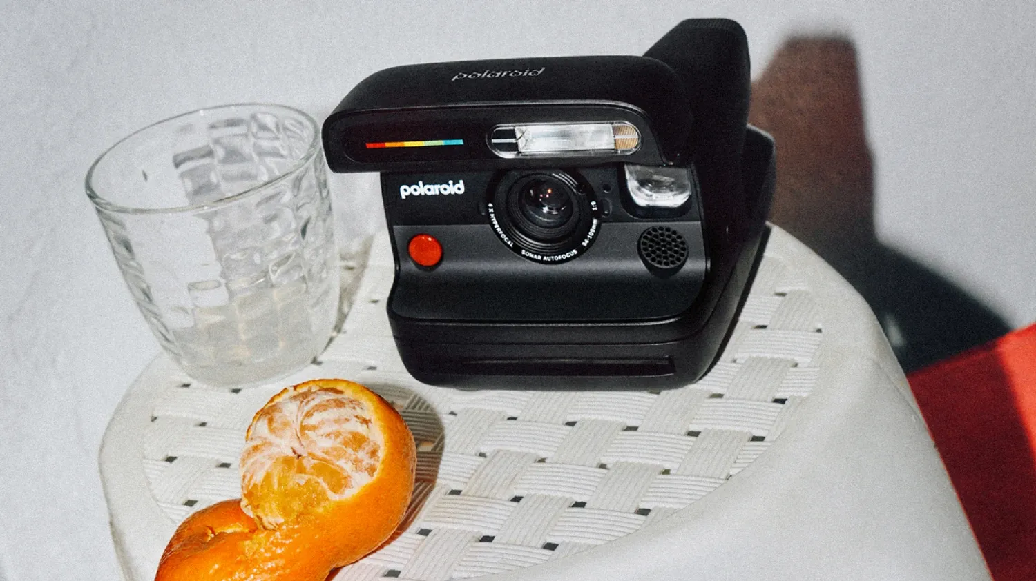The Black Polaroid Flip on a seat with a glass of water and a half-peeled mandarin