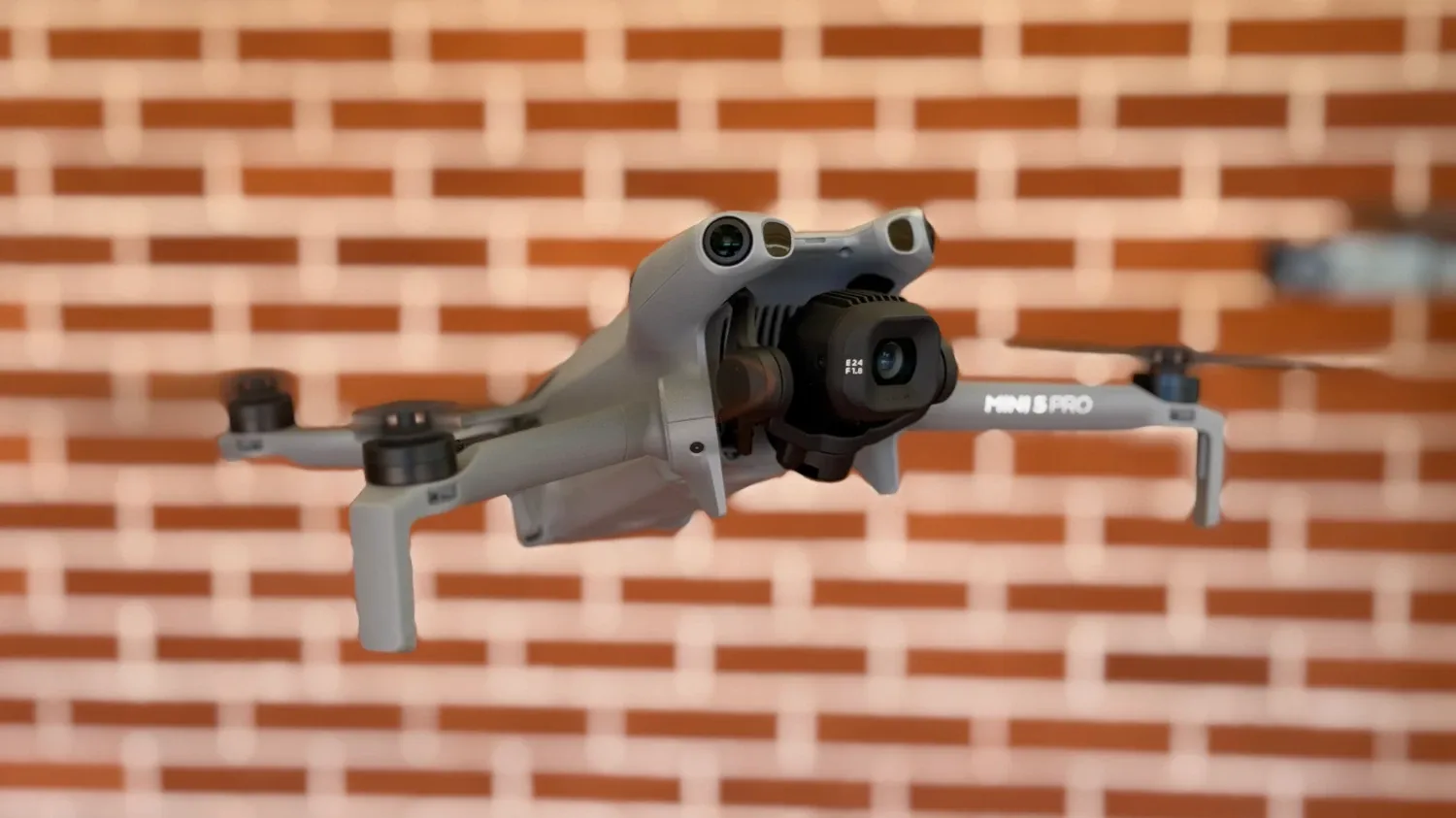 The DJI Mini 5 Pro hovering in front of a brick wall