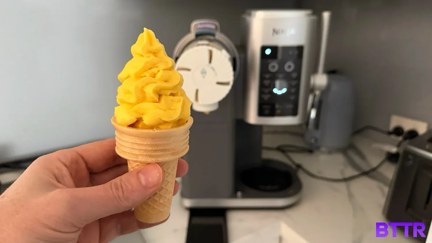 Holding a soft serve fruit whip in front of the Ninja Swirl by CREAMi