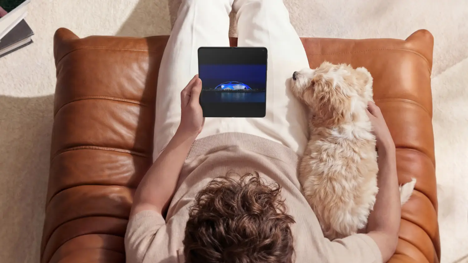 A top down view of a man looking atthe OPPO Find N6 with his dog in the chair with him.